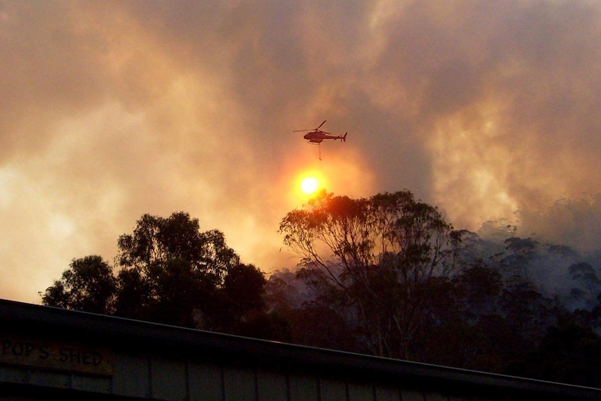 A water-bombing helicopter flies through smoke from a bushfire in Bicheno.