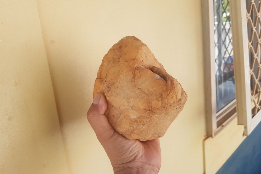 A person's hand holding a large yellow rock