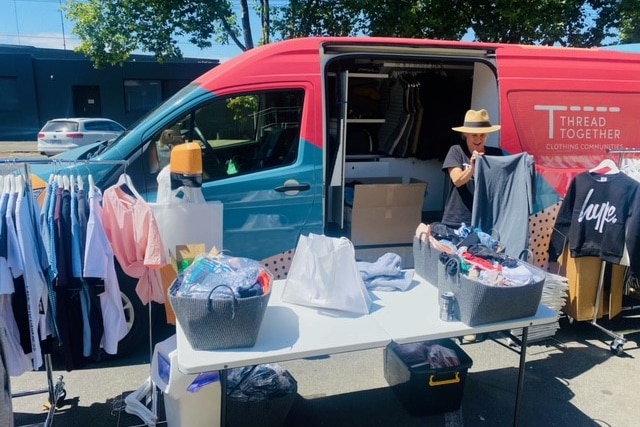 A colourful van with the door open, and tables with boxes of clothes on them, and clothes on hangers