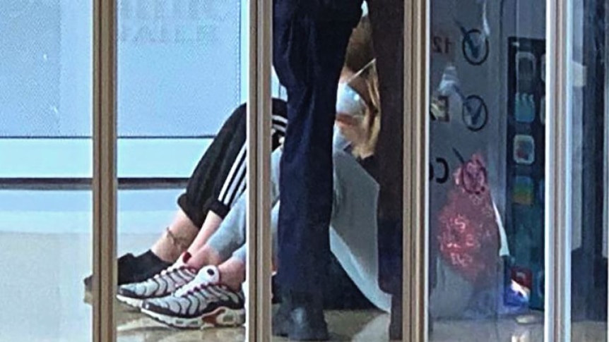 Police stand next to two girls sitting on the ground.