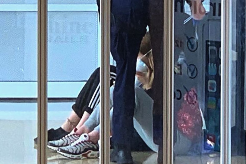 Police stand next to two girls sitting on the ground.