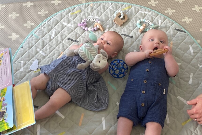 Two newborn babies on the floor surrounded by toys.