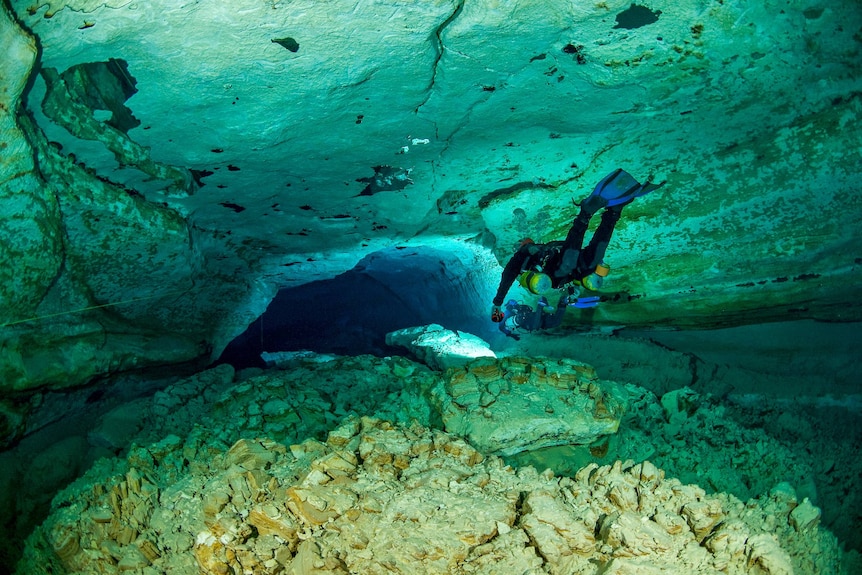 A scuba diver floats through an underwater tunnel.