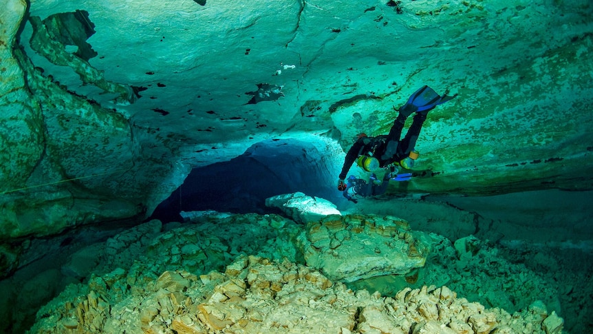 A scuba diver floats through an underwater tunnel.