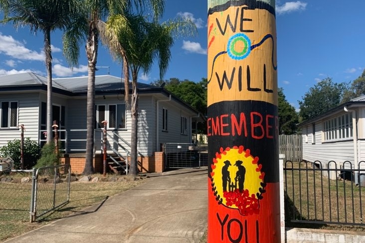 A power pole painted with a sunset the words we will remember you and an Aboriginal flag and two Anzacs