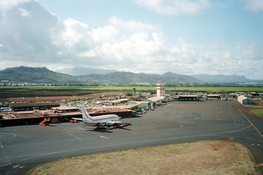 An aerial photograph of an airport with one plane parked and mountains in the background.