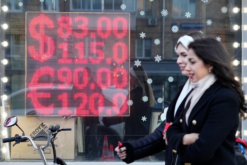 People walk past a currency exchange office displaying the exchange rates for roubles against US dollars and euros