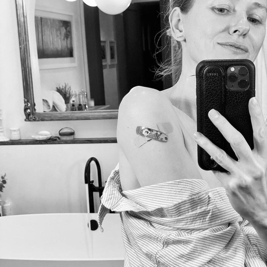 A beautiful actress takes a selfie in from of a mirror showing her covid-19 vaccination bandaid.