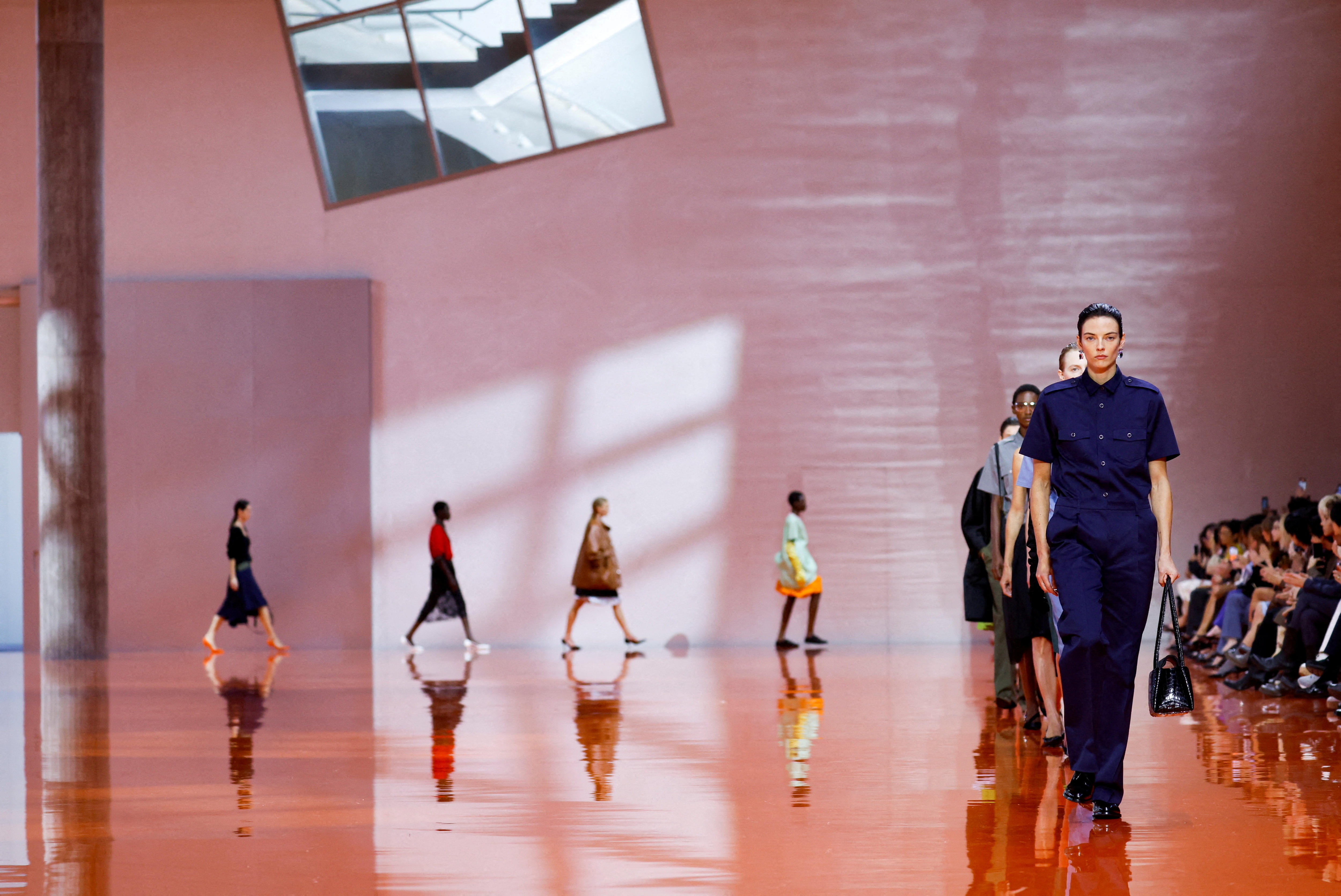 Una fila de modelos camina por una pasarela sobre un fondo rosa