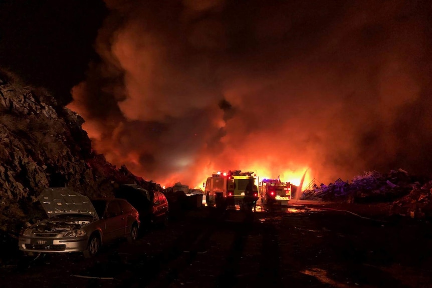 Fire trucks, illuminated by fire, spray water.