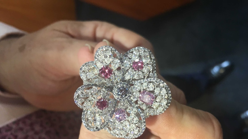 Man hand holding 'Blossom' diamond ring featuring Argyle pink diamonds surrounded by white diamonds. In shape of flower petals