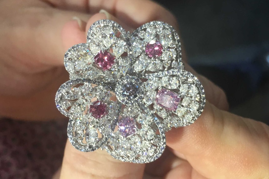 Man hand holding 'Blossom' diamond ring featuring Argyle pink diamonds surrounded by white diamonds. In shape of flower petals