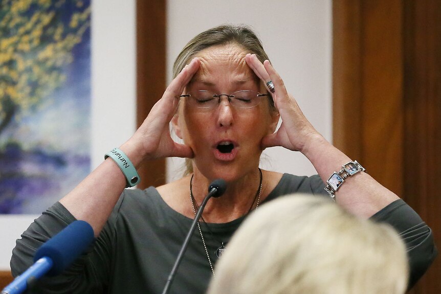 White woman Scarlett Lewis speaks into a courtroom microphone with her eyes closed and hands on her head.