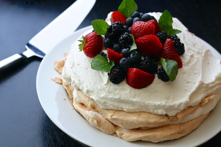 A big pavlova topped with whipped cream, strawberries, blackberries and blueberries and mint leaves.