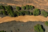 An aerial shot of a dry brown river in Greenough, the Midwest. There's a tiny green car at the mouth.