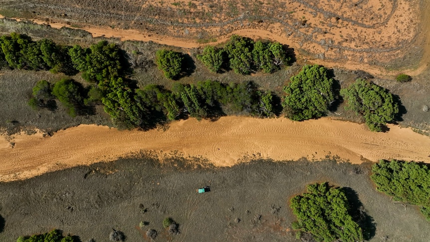 An aerial shot of a dry brown river in Greenough, the Midwest. There's a tiny green car at the mouth.