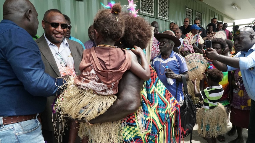 A man smiles as he greets and woman and child amid a crowd of people