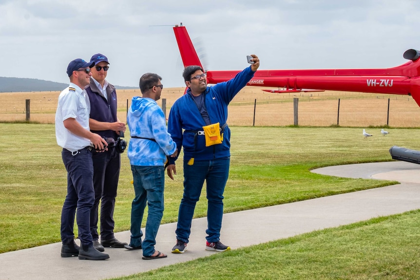 Two tourists take a selfie with two Twelve Apostles Helicopters staff members