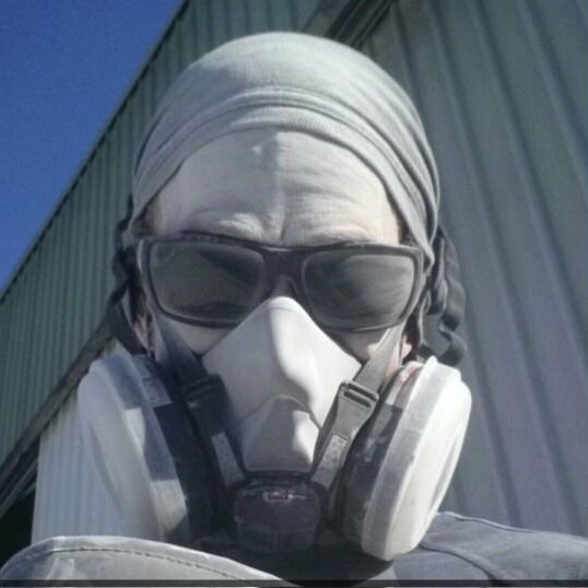 Duane Calvey wearing a fitted respirator mask is covered with white silica powder.