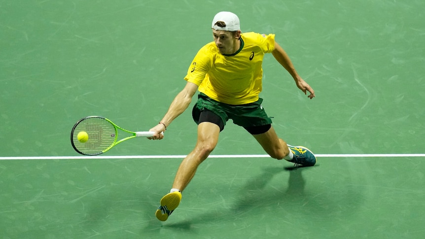 An Australian men's tennis player stretches his body as he leans forward to hit a forehand volley in a Davis Cup 