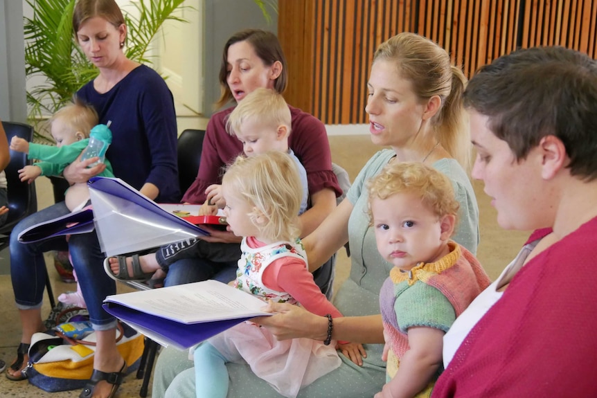 A group of mothers and their children sit singing in a choir.