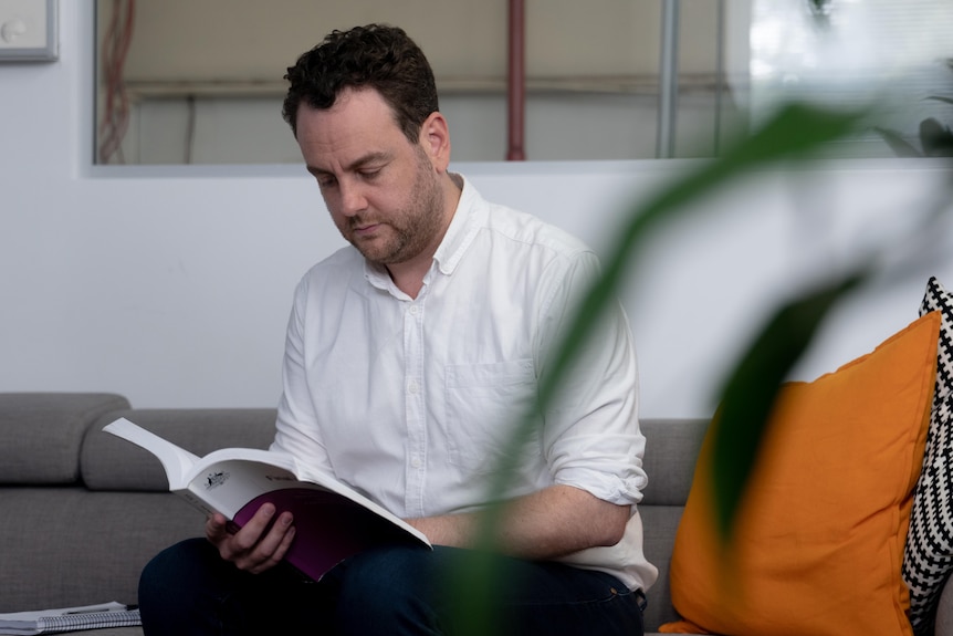 A man in a white shirt reads through papers as he sits on a couch.