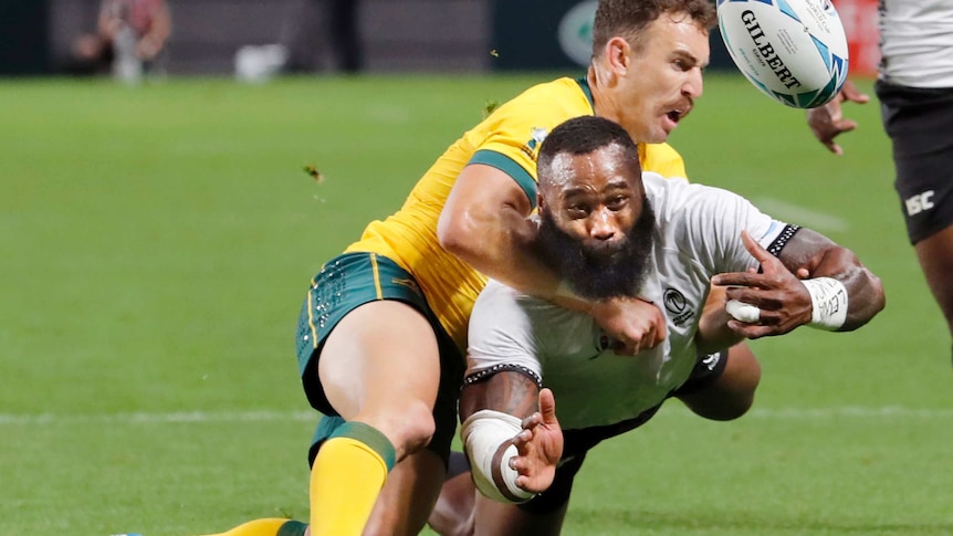 Semi Radradra, in white, is tackled by Nic White, in gold, whilst throwing the ball
