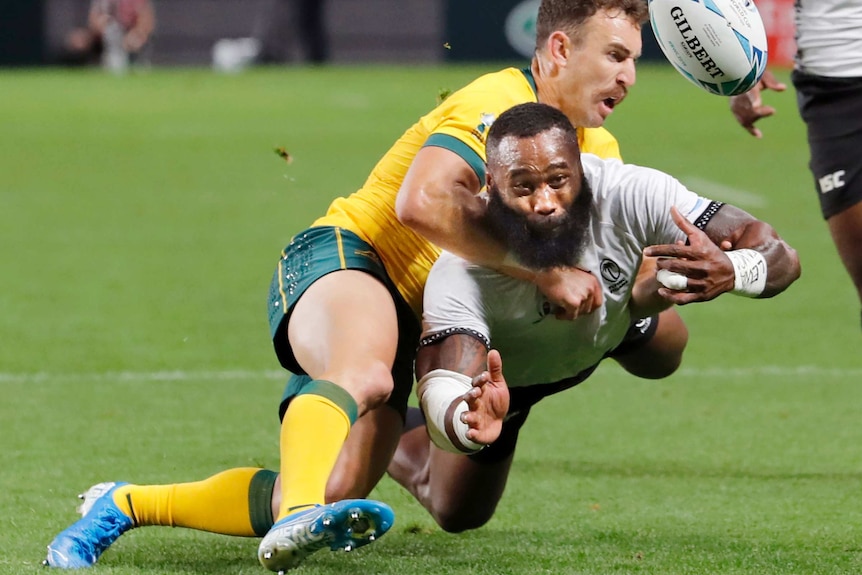 Semi Radradra, in white, is tackled by Nic White, in gold, whilst throwing the ball