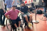 Two men in wheelchairs positioned in front of TV crews 
