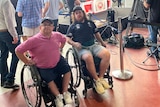 Two men in wheelchairs positioned in front of TV crews 