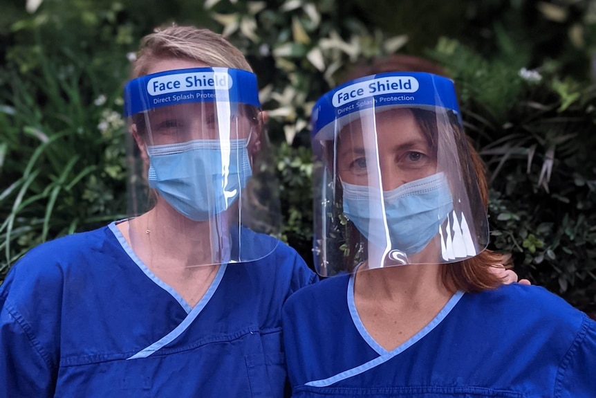 Two doctors wear scrubs and face shields