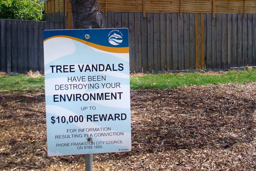 A Frankston Council sign, in front of a damaged tree, offers $10,000 reward for information about tree vandals