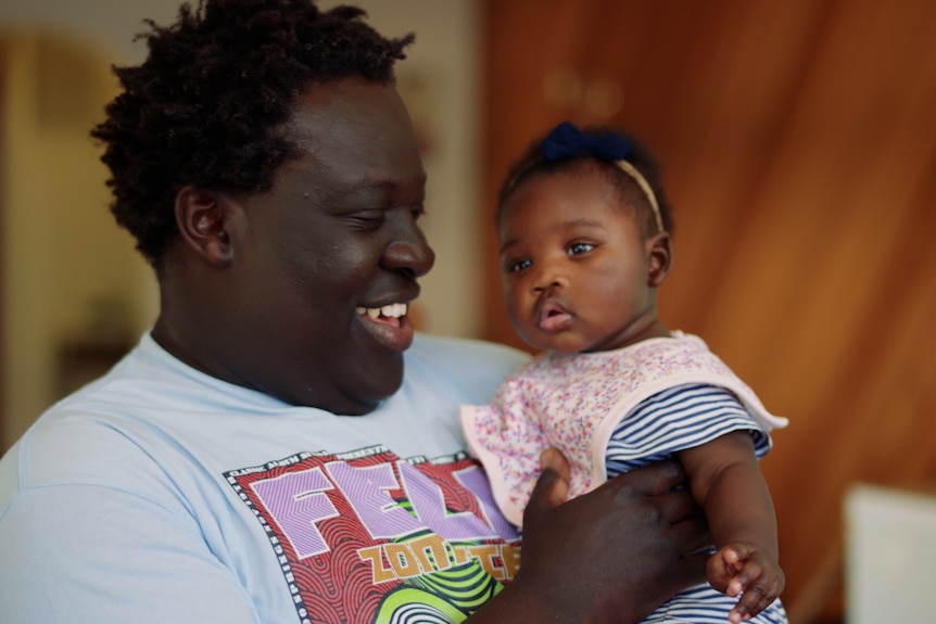 Man holds baby in his arms, looking at her and laughing. 