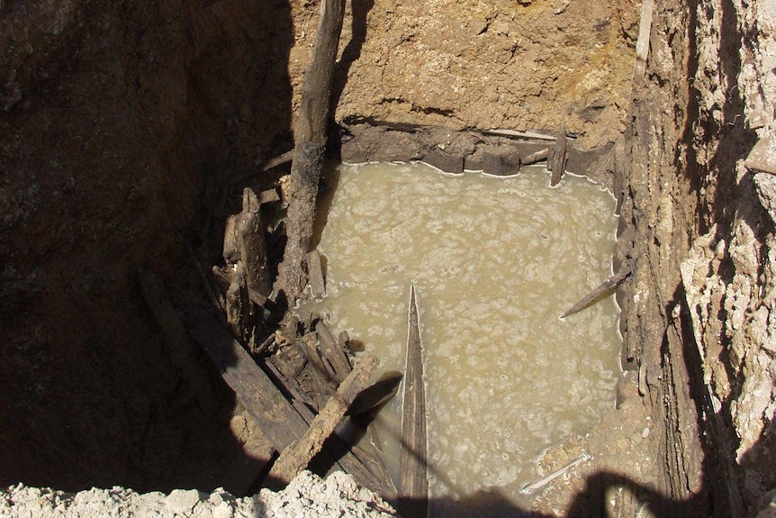 An aerial view of a caved-in mine shaft filled with water.