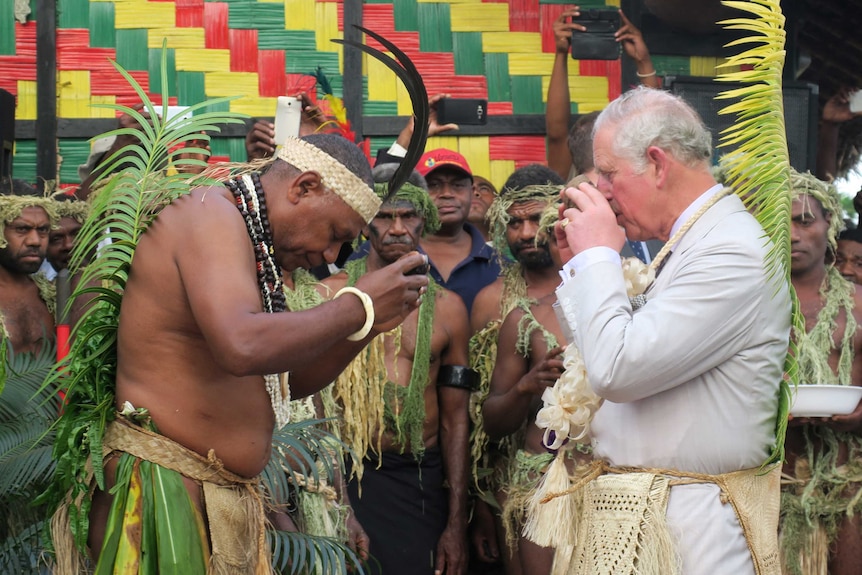Prince Charles is taking part in a traditional ritual in Port Vila, Vanuatu, drinking something while Vanuatuans watch.