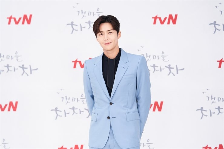 A man in a blue suit stands in front of a promotional sign for tvN.