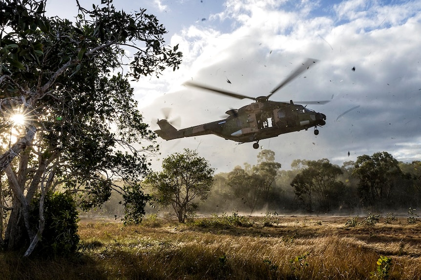 Military Helicopter landing in bush setting sending sticks and dirt flying