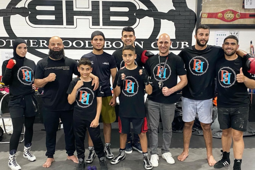 A group of boys, men, and a woman all stand together and smile at the camera.