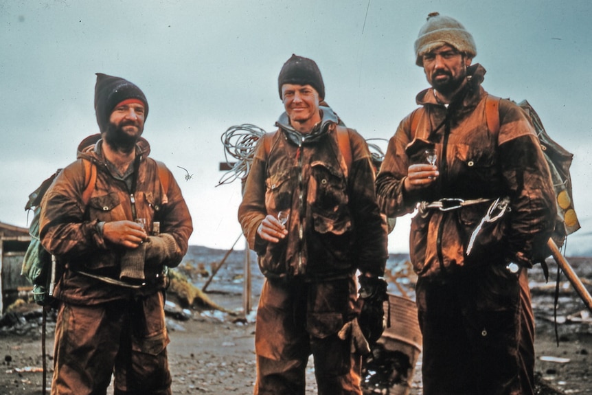 An old photograph of three men on Heard Island, dressed in cold weather gear.