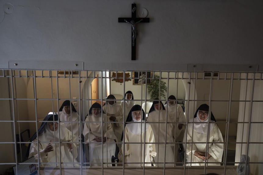 Un grupo de monjas se sientan juntas detrás de un frontón de hierro blanco para hablar con la prensa. 