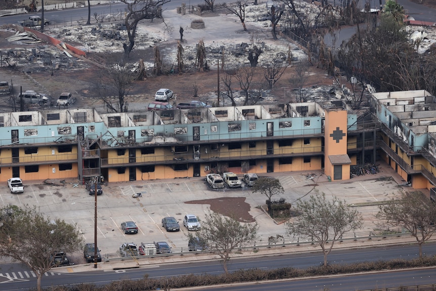 An aerial shot shows the shell of a burnt-out hotel or apartment building 