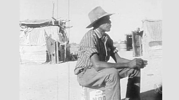 Indigenous man in hat sits at outback station