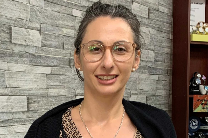 A woman wearing glasses stands behind a jewellery store counter