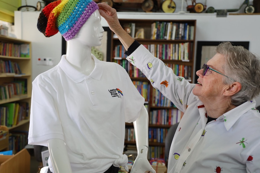 A silver-haired woman adjusts a rainbow beanie on top of a mannequin