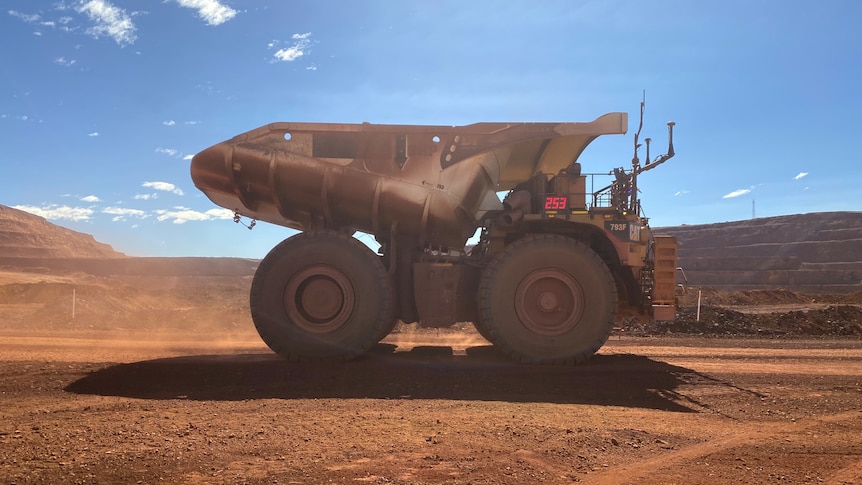 Mining truck drives on red dirt at BHP's Jimblebar mine on a bright sunny day. 