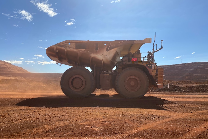 Mining truck drives on red dirt at BHP's Jimblebar mine on a bright sunny day. 