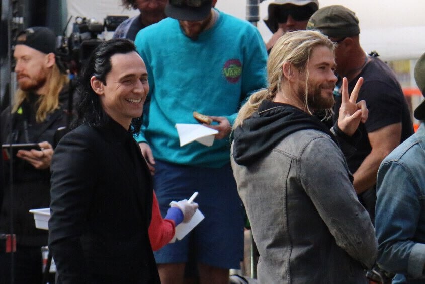 Tom Hiddleston and Chris Hemsworth smile at onlookers