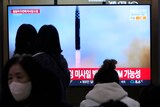 People watch a TV screen which shows a missile launching. 