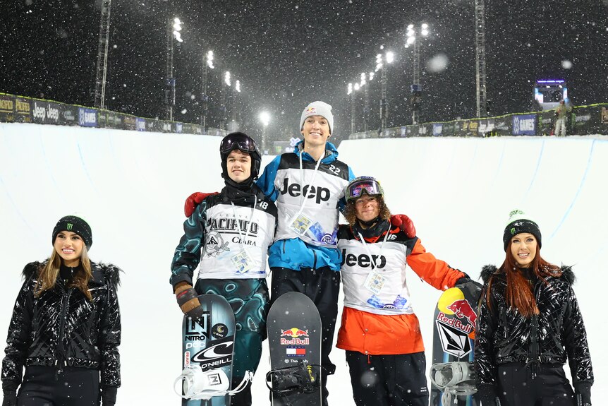 Scotty James (centre) and Val Guseli (right) stand on a podium in front of a flood-lit halfpipe. 
