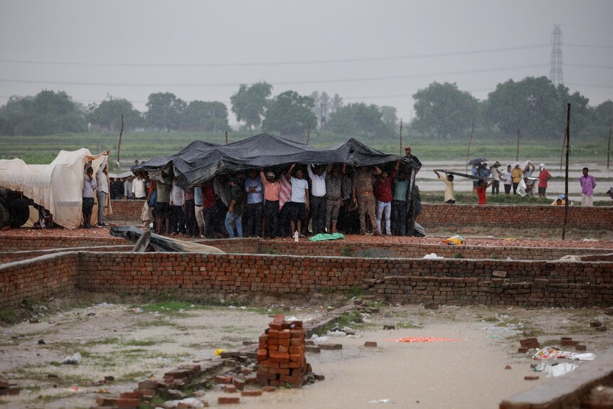 People take shelter under a tarp in a muddy field.